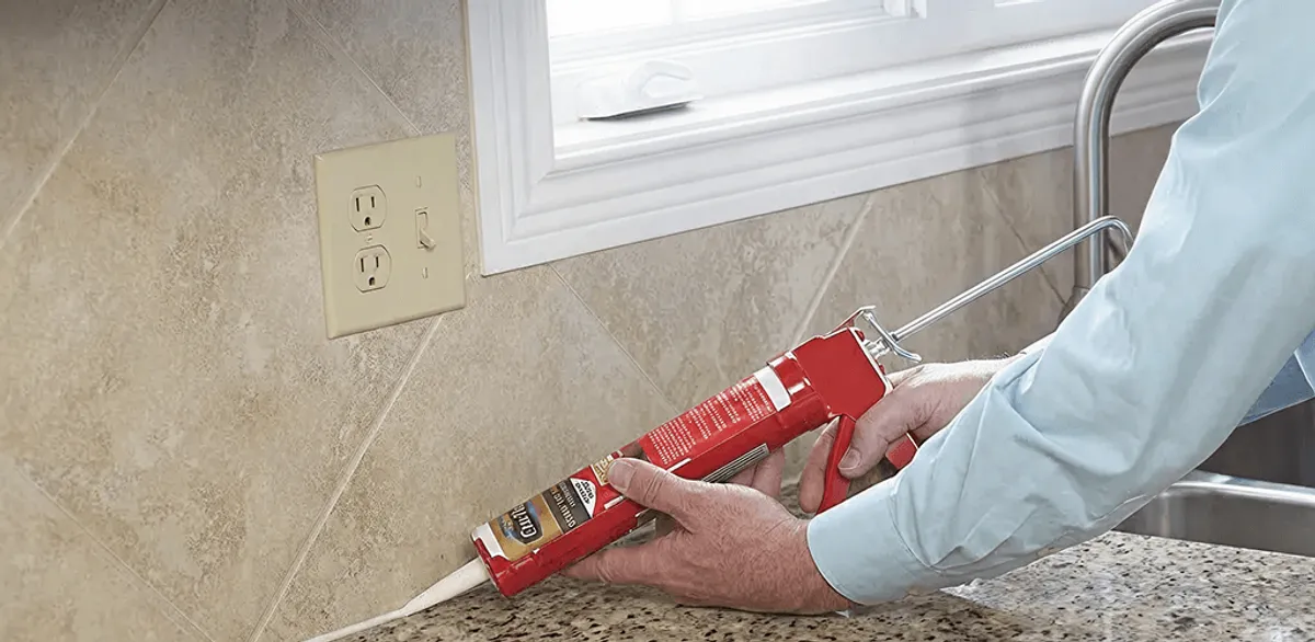 Handyman applying caulk along a kitchen backsplash and countertop seam in Gilbert, AZ