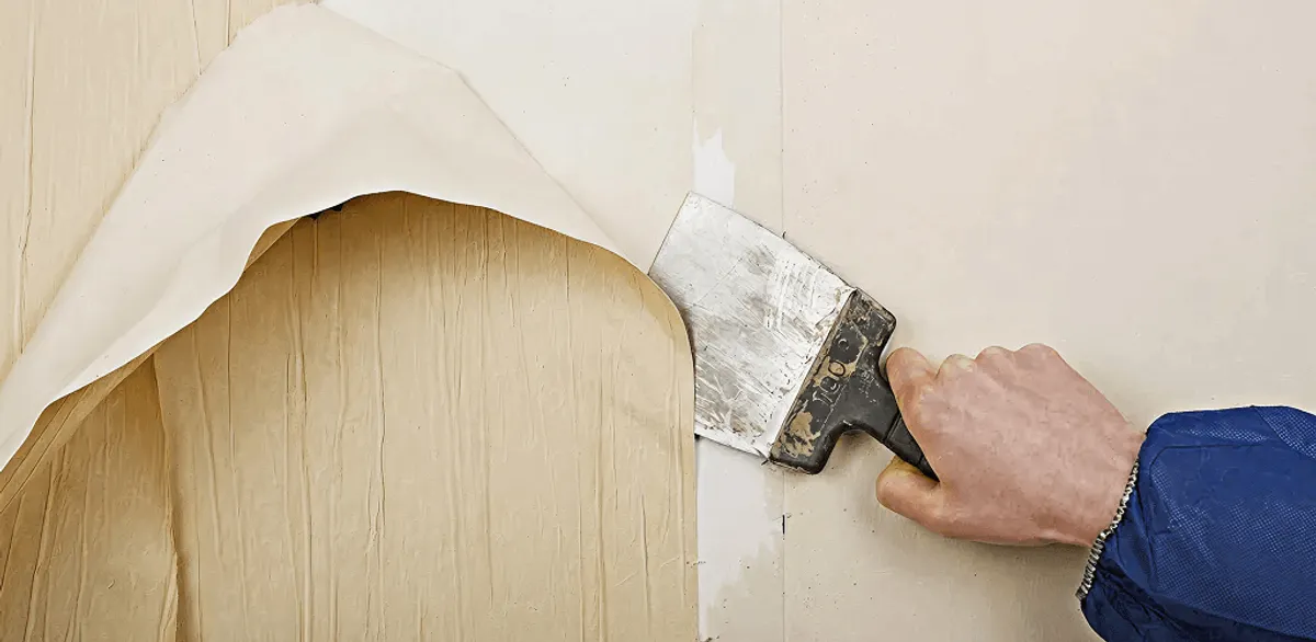 Handyman removing wallpaper with a scraper for wall preparation in Gilbert, AZ