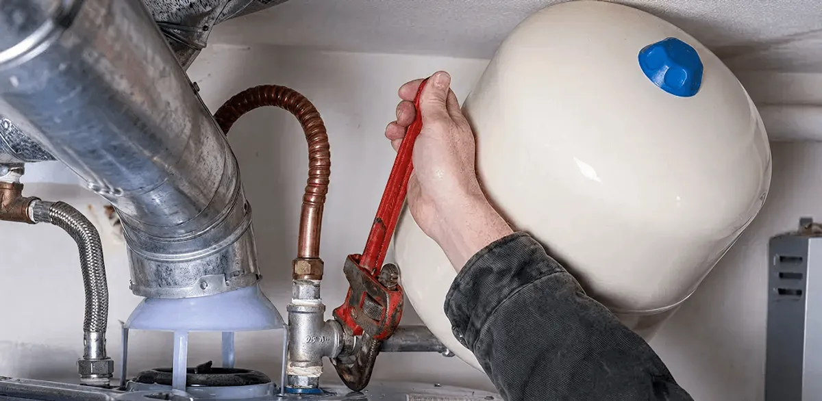 Water heater repair technician tightening plumbing connections near a tank unit in Gilbert, AZ